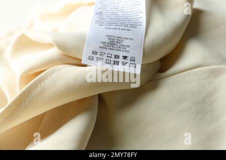 Clothing label with care instructions on beige garment, closeup Stock Photo