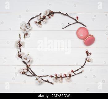 Decorative frame of flowers and macaroons on a white wooden background. Almond biscuits and branches of flowering apricots. Template for design. Flat Stock Photo