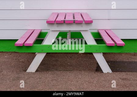 Colourful table and bench painted in bright white, pink and green against a the side of a building painted the same. Stock Photo