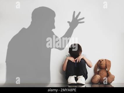 Child abuse. Father yelling at his son. Shadow of man on wall Stock Photo