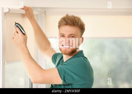 Handyman with cordless screwdriver installing roller window blind indoors Stock Photo