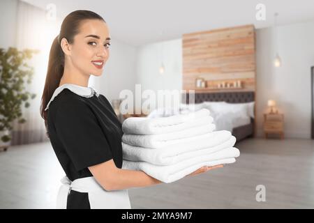 Beautiful chambermaid with clean folded towels in hotel room Stock Photo