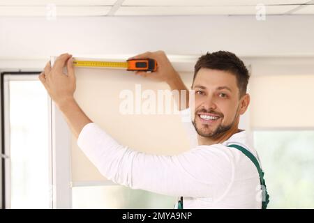 Handyman with tape measure installing roller window blind indoors Stock Photo