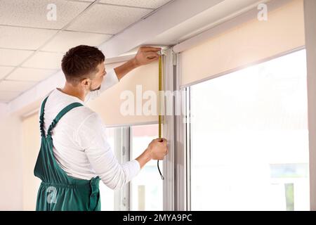 Handyman with tape measure installing roller window blind indoors Stock Photo