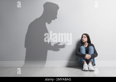 Child abuse. Father yelling at his daughter. Shadow of man on wall Stock Photo