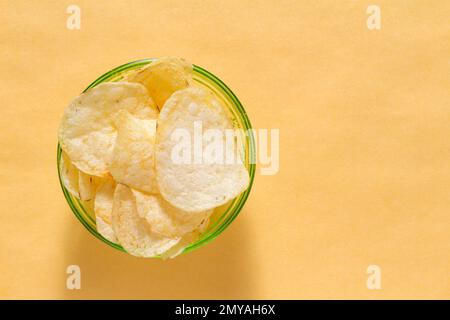 Lots of potato chips in container on yellow background Stock Photo