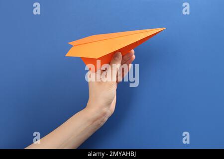 Woman holding paper plane on blue background, closeup Stock Photo
