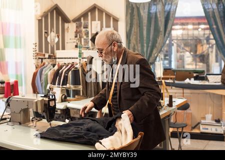 A gray-haired man works at a sewing machine in his atelier Stock Photo