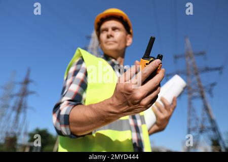 Professional electrician near high voltage tower, focus on hand with portable radio station Stock Photo