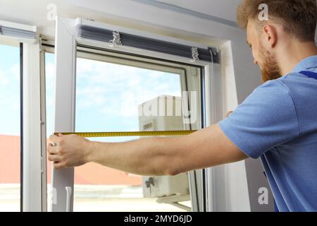 Handyman with tape measure installing window blinds indoors Stock Photo