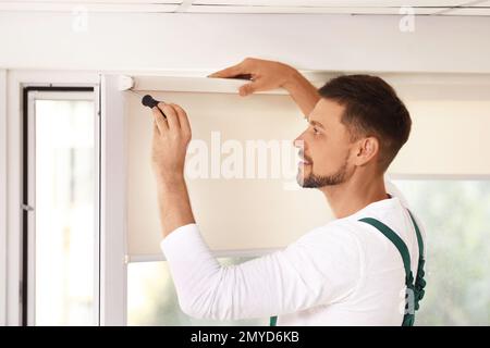 Handyman with screwdriver installing roller window blind indoors Stock Photo