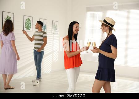 Young women with glasses of champagne at exhibition in art gallery ...
