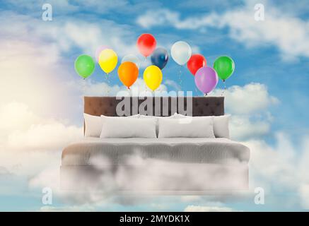 Sweet dreams. Bed with bright air balloons in blue cloudy sky Stock Photo