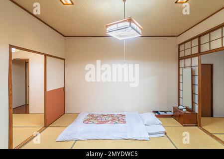 A typical traditional Japanese bedroom characterized by tatami mats, shoji doors, fusuma walls, futon mattress and minimalist decorations, creating a Stock Photo