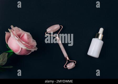 White cosmetic bottle, facial roller and pink rose flower on black background. Natural cosmetics, skin care concept. Top view, flat lay. Stock Photo