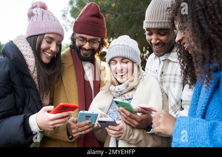 Group of young mixed race friends with mobile phones. Technology addicted people using colorful cell Stock Photo