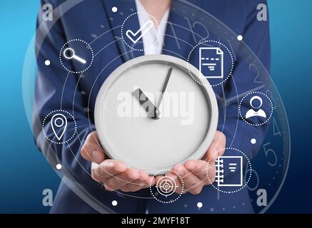 Time management concept. Woman holding clock surrounded by icons, closeup Stock Photo