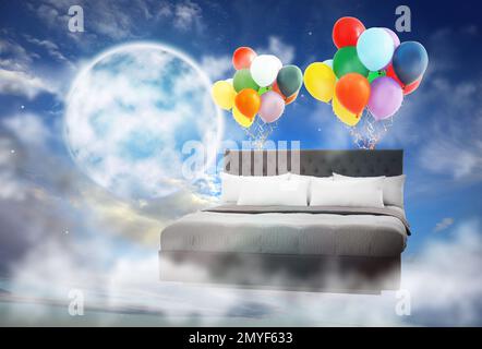 Sweet dreams. Bed with bright air balloons near full moon in cloudy sky Stock Photo