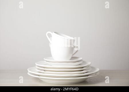 Stack of clean plates and cups on table against white background Stock Photo