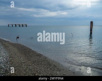 Reinforced concrete pile sticking out of the water. Remains of an old bridge in the sea. Ruined pier. Abandoned. Armature at sea. Destroyed building. Stock Photo