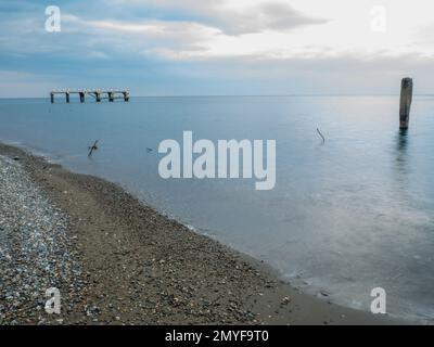 Reinforced concrete pile sticking out of the water. Remains of an old bridge in the sea. Ruined pier. Abandoned. Armature at sea. Destroyed building. Stock Photo