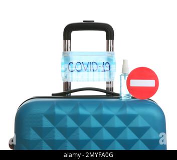 Antiseptic spray, stop sign and protective mask with inscription COVID-19 on suitcase against white background. Travel restriction during coronavirus Stock Photo