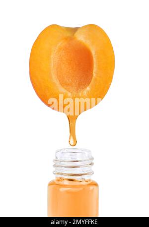 Apricot oil dripping from fresh fruit half into glass bottle on white background
