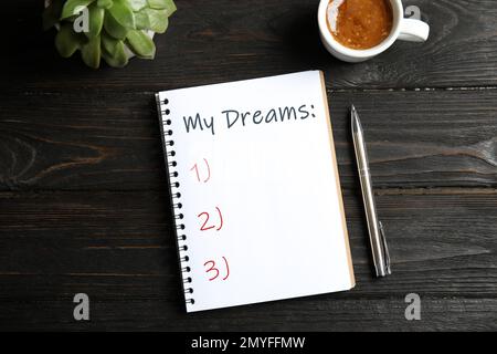 Notebook with dreams list on dark wooden table, flat lay Stock Photo