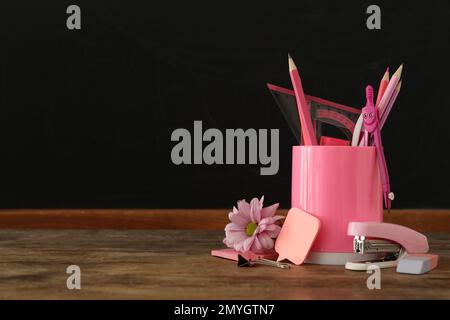 Set of stationery and flower on wooden table near chalkboard, space for text. Teacher's Day Stock Photo