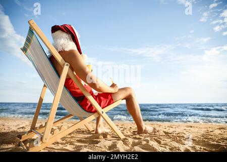 Santa Claus relaxing in chair on beach, space for text. Christmas vacation Stock Photo