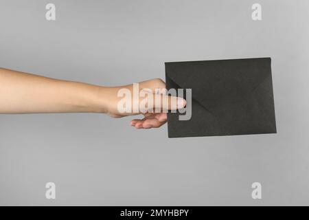 Woman holding black paper envelope on light grey background, closeup Stock Photo