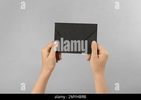 Woman holding black paper envelope on light grey background, closeup Stock Photo
