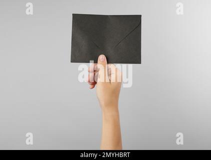 Woman holding black paper envelope on light grey background, closeup Stock Photo