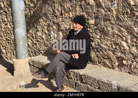An elderly man watched the activities of his Northern Iraqi town from his perch on a cement bench leaning against a stone wall. Stock Photo