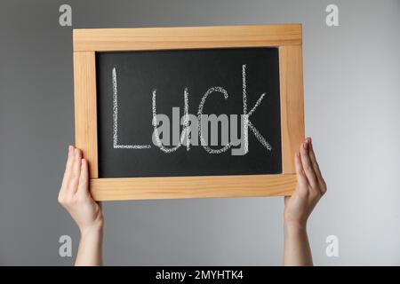Woman holding blackboard with word LUCK on light grey background, closeup Stock Photo