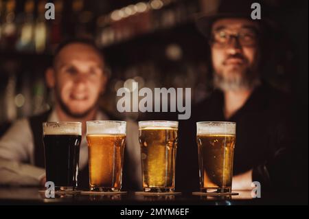 four glasses with different beers on bar counter in pub against the background of bartenders Stock Photo