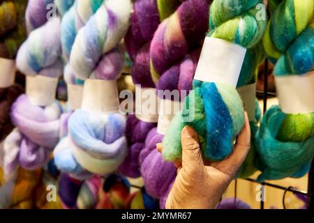 A crafter chooses a multicolored wool yarn from the many skeins on a display rack. Stock Photo