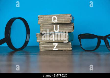 A magnifying glass, glasses and a stack of book written with Quiz on a blue background. Stock Photo