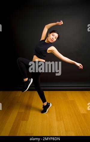 Young Asian Dancer Throwing Arms in the Air in Front of Black Backdrop Stock Photo