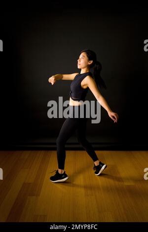 Young Asian Dancer Throwing Arms in the Air in Front of Black Backdrop Stock Photo