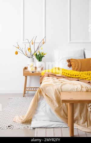 Vases with tree branches, Easter eggs and flowers on table in room ...