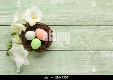 Nest with beautiful Easter eggs and freesia flowers on color wooden background Stock Photo