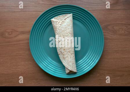 A folded wholegrain wrap on a green plate. Stock Photo