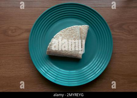 A folded wholegrain wrap on a green plate. Stock Photo