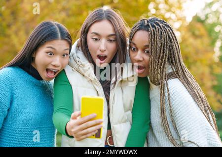 Three surprised friends using a mobile outdoors Stock Photo