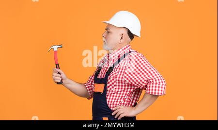 Side view of serious middle aged carpenter using spray gun for painting  wood detail with white