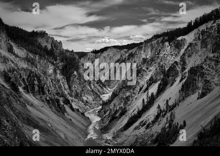 A high angle of a river flowing through a valley of mountains shot in grayscale Stock Photo