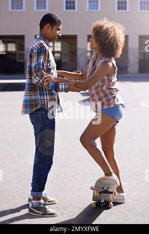 Let me show you. a young man teaching his girlfriend how to skateboard. Stock Photo