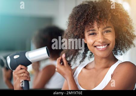 Im having a great hair day. Cropped portrait of a young woman blow drying her hair in the bathroom. Stock Photo
