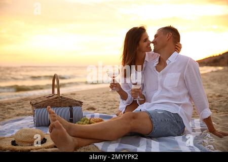 Lovely couple having romantic picnic on beach at sunset Stock Photo